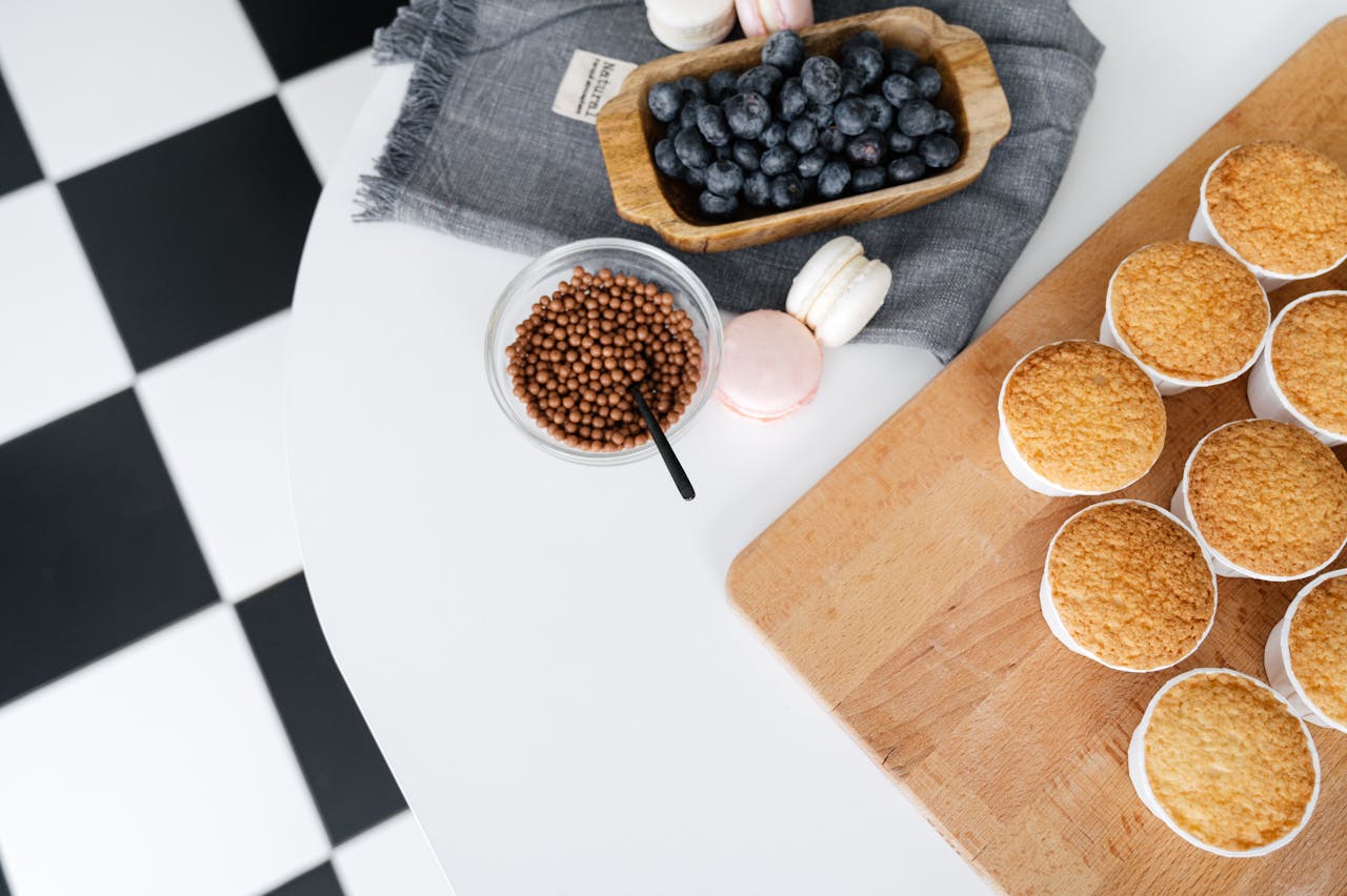 Top view of a dessert setup with blueberries, macarons, and cupcakes on a wooden tray.