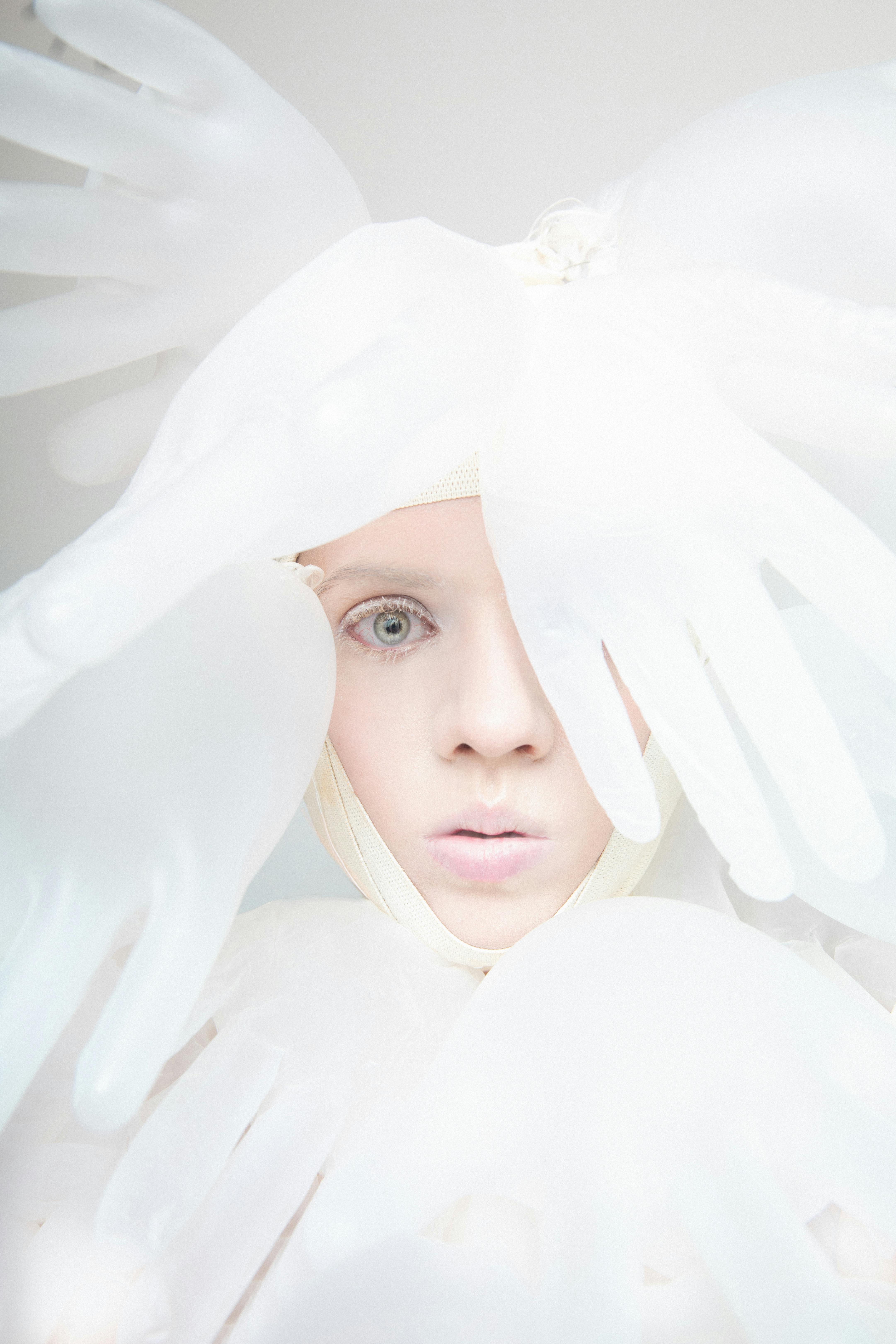 A creative portrait featuring a woman surrounded by white latex gloves on a bright background.